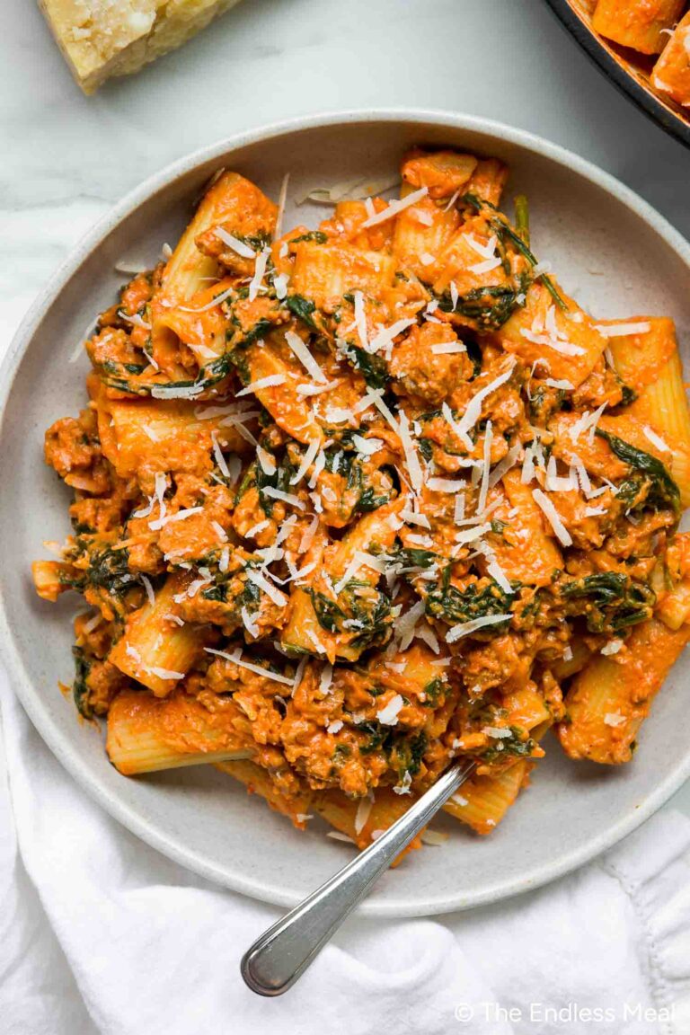 A plate of rigatoni goat cheese tomato pasta with creamy sauce, ground meat, spinach, and grated cheese, served with a fork.