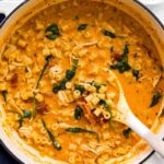 A pot of creamy tomato pasta with diced chicken, spinach, and small tube-shaped noodles, stirred with a white spoon—like a cozy Marry Me Chicken Soup reimagined as a hearty pasta dish.