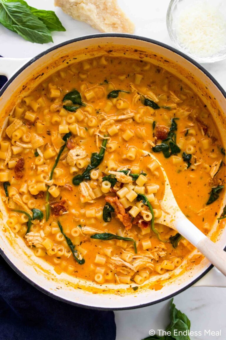 A pot of creamy tomato pasta with diced chicken, spinach, and small tube-shaped noodles, stirred with a white spoon—like a cozy Marry Me Chicken Soup reimagined as a hearty pasta dish.