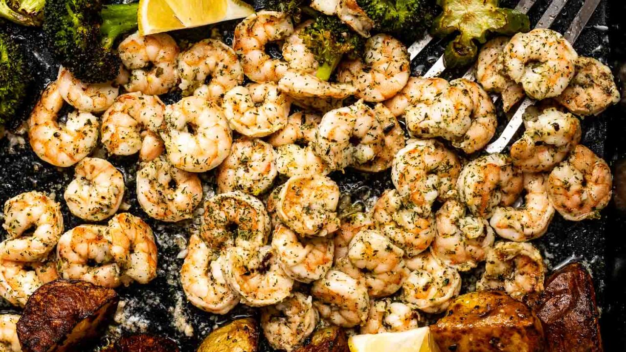 A sheet pan filled with roasted broccoli, seasoned shrimp, and golden potatoes, all garnished with fresh lemon wedges.