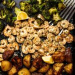 A sheet pan filled with roasted broccoli, seasoned shrimp, and golden potatoes, all garnished with fresh lemon wedges.