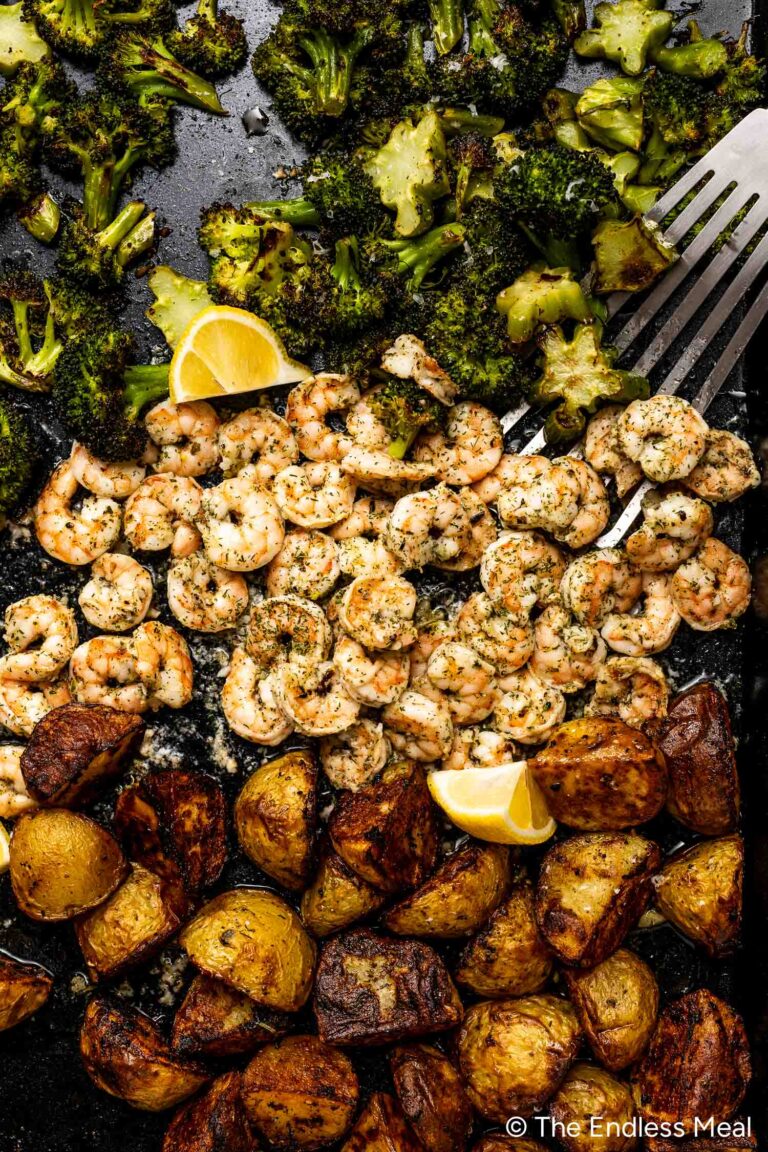 A sheet pan filled with roasted broccoli, seasoned shrimp, and golden potatoes, all garnished with fresh lemon wedges.